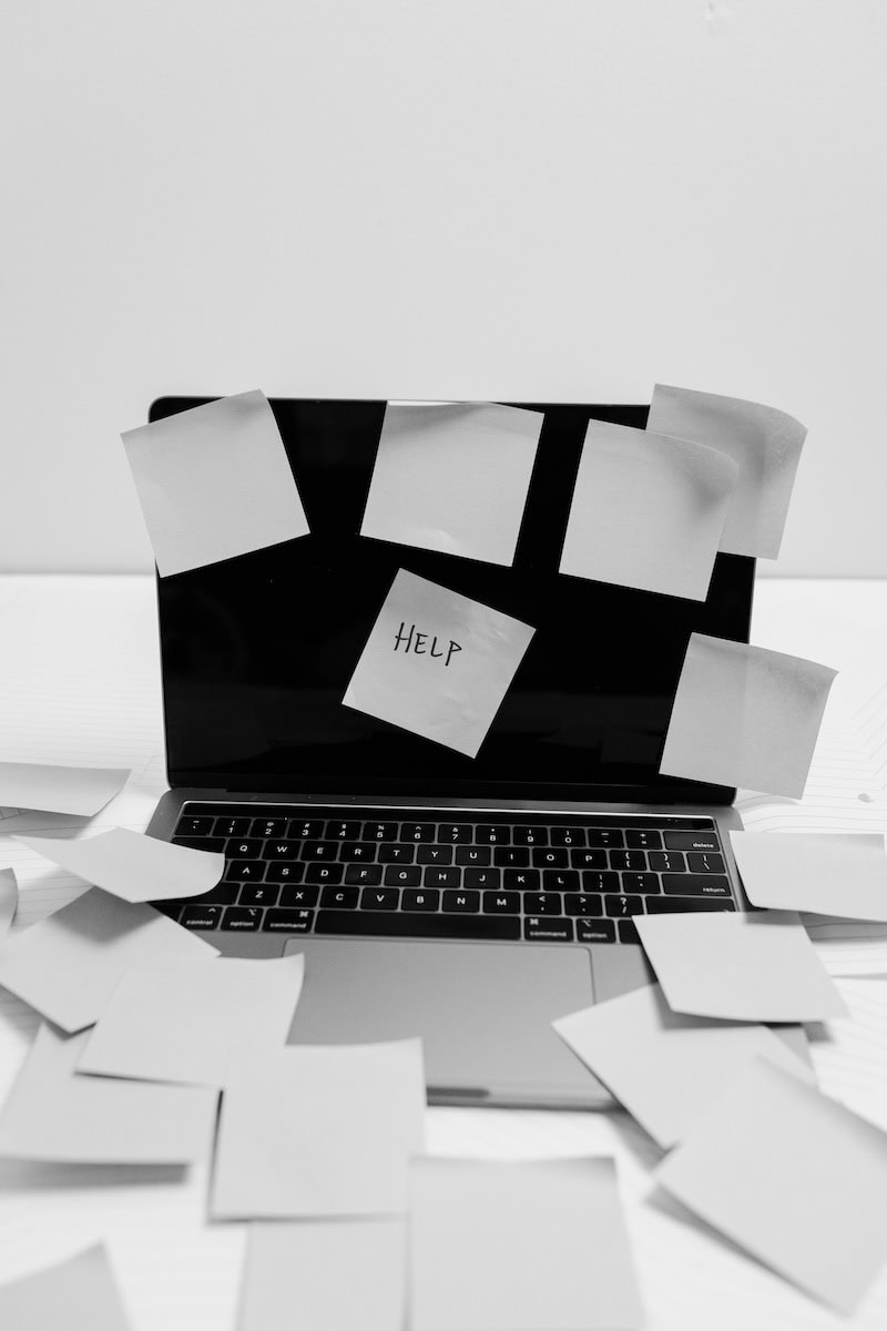 Svartvit bild på en laptop som är full med post-it och ordet "help" på en av dem. 