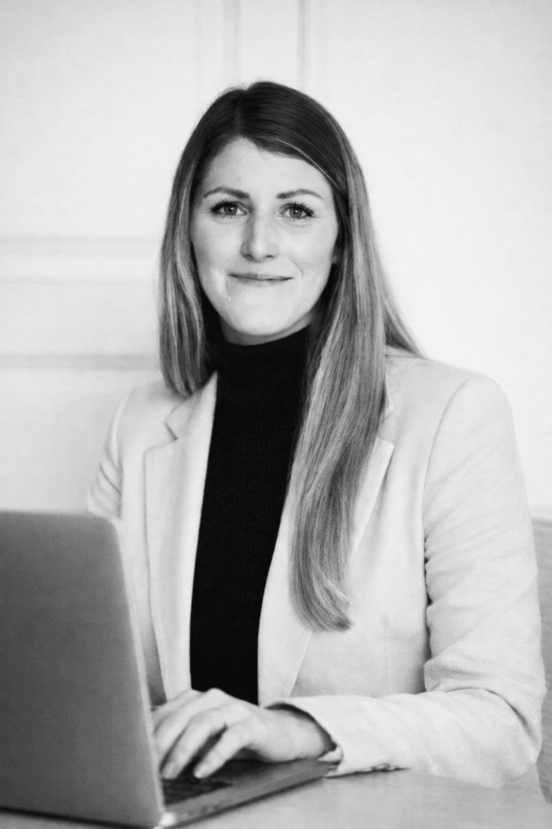 Anna, webbdesigner på Pinecone, sitter vid ett skrivbord iklädd svart polo och ljus kavaj. Hon tittar in i kameran och ler med en laptop framför sig.